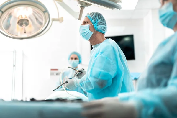 Cirujano en máscara protectora usando laparoscopio durante operación quirúrgica — Foto de Stock