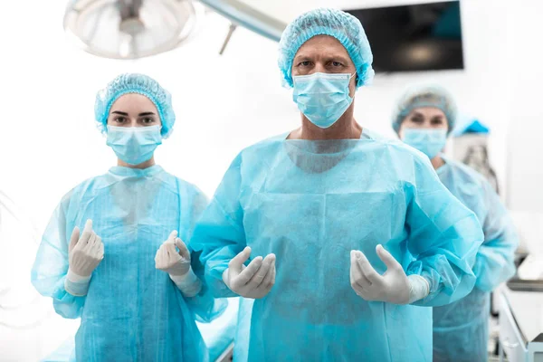 Cerrah ve yardımcıları ameliyat odasında duran steril mavi önlük içinde — Stok fotoğraf