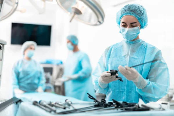 Enfermera joven en vestido azul sosteniendo instrumento laparoscópico — Foto de Stock