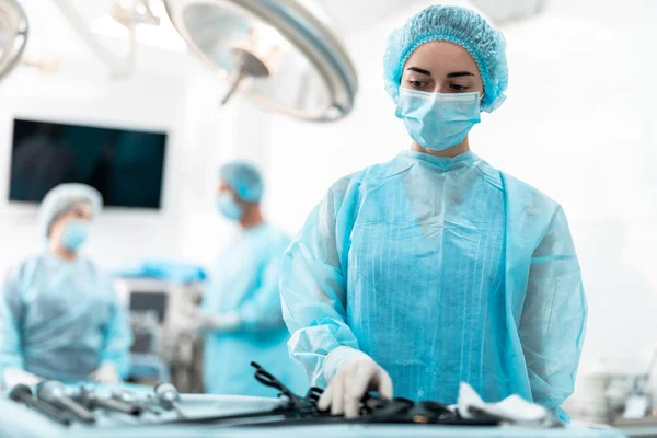 Enfermera joven en bata azul de pie cerca de la mesa con herramientas laparoscópicas — Foto de Stock