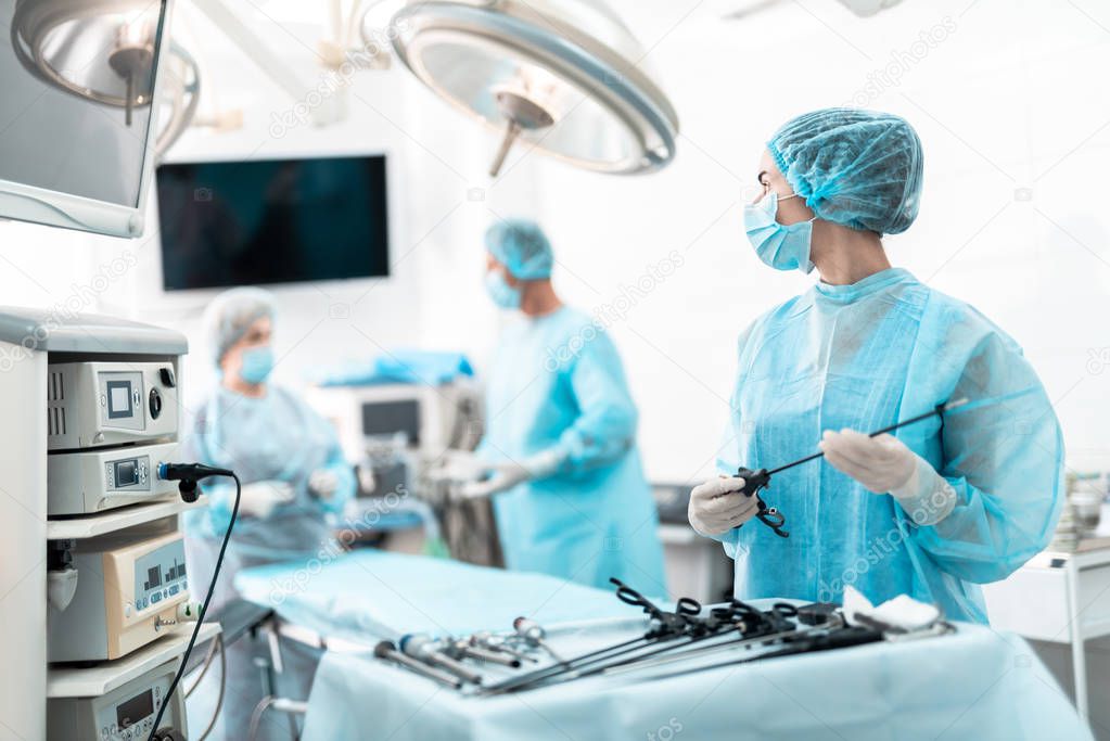 Young nurse holding laparoscopic instrument and looking at colleagues
