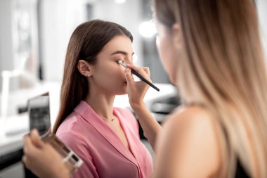 Visagiste holding paleti özel fırçası ile güzel bayan için makyaj yaparken gölgeler