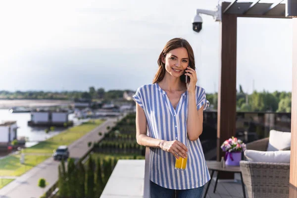 Waist up portrait of young woman standing on balcony and speaking on handy. She looking at camera with smile. Copy space on left side