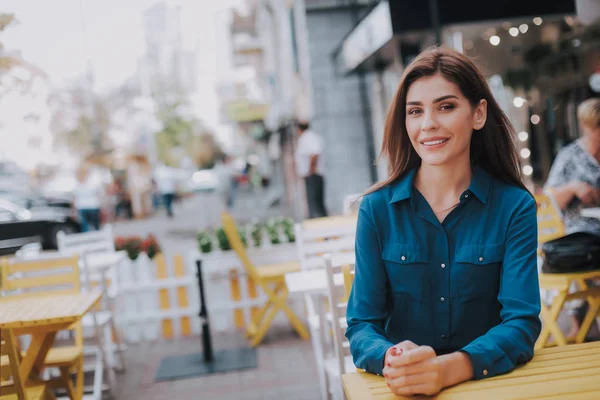 Concept of success and well-being. Waist up portrait of smiling business lady sitting in cozy outdoor cafe. Copy space on left