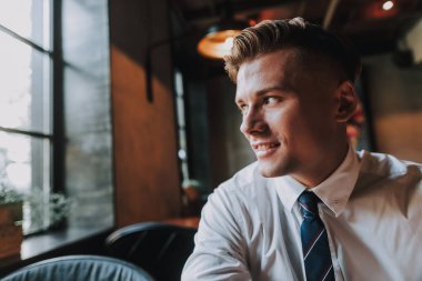 Başarı ve refah kavramı. Portre rahat kafede oturan ve penceresine bakarak yakışıklı gülümseyen iş adamı kapatın. Kopya alanı solda