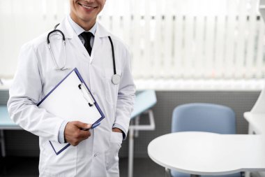 Beyaz tıbbi giyim eşyası ve Pano basılı tutup, boynunda steteskop sahip iken gülümseyen neşeli duygusal doktor