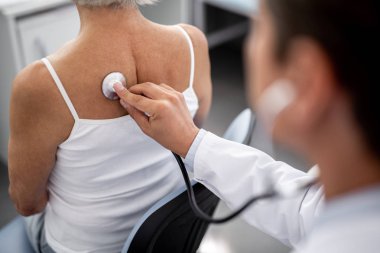 Kadının oturmak ve sağlık durumu denetlenirken stetoskop tutan dikkatli özenli Uygulayıcı