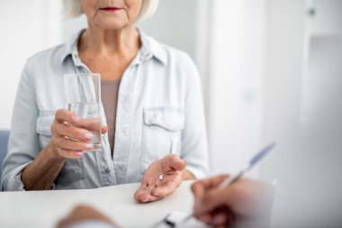 Onun doktoru ziyaret ve hapları alırken bir bardak su tutarak sakin yaşlı Bayan