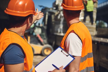 El koyarak ve duran üniformalı Oluşturucusu yanındaki bina süreci işaret eden turuncu kask içinde deneyimli ustabaşı