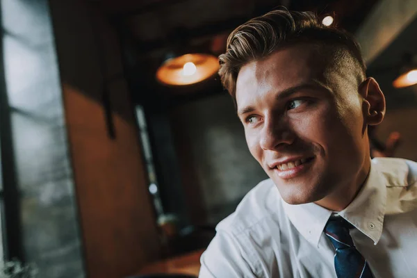 Concept of success and positive mind. Close up portrait of handsome smiling businessman looking on window while sitting in cafe. Copy space on left