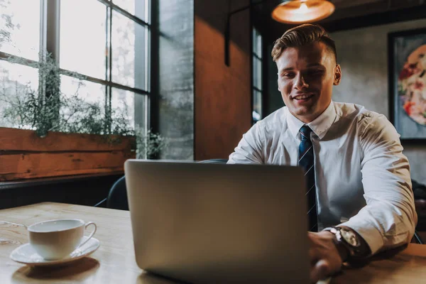 Успешный улыбающийся мужчина сидит с ноутбуком в кафе — стоковое фото