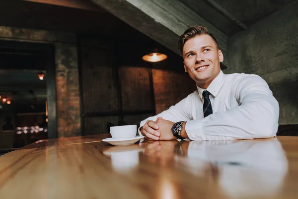 Concept of success and well-being. Low angle portrait of handsome smiling businessman sitting in luxury cozy cafe with cup of coffee. Copy space on left