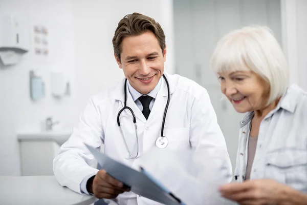 Médico feliz e seu paciente sorridente olhando para a área de transferência — Fotografia de Stock