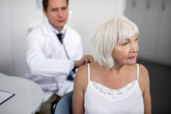 Yaşlı kadın onun uygulayıcı stetoskop kullanarak süre mesafe bakarak — Stok fotoğraf