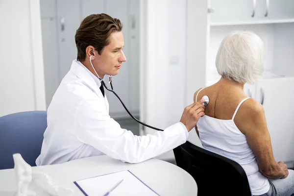 Klid doktor na sobě stetoskop a posuzování pacienta — Stock fotografie