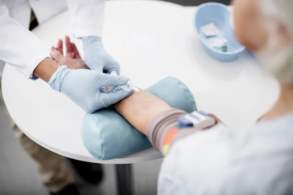 Κοντινό πλάνο της βελόνας στην βραχίονα του ασθενούς και τα χέρια του γιατρού κρατώντας το — Φωτογραφία Αρχείου