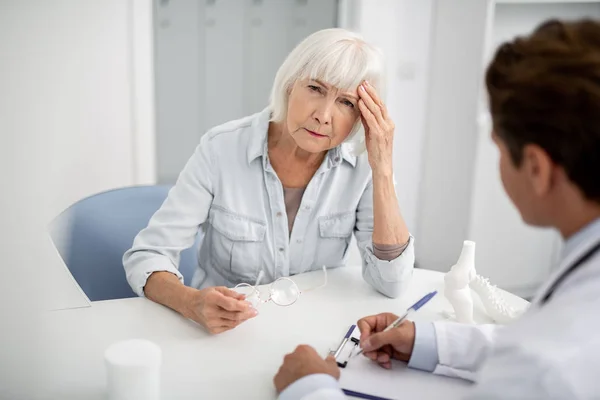 Having baş ağrısı ve Doktor önünde oturan mutsuz Bayan — Stok fotoğraf