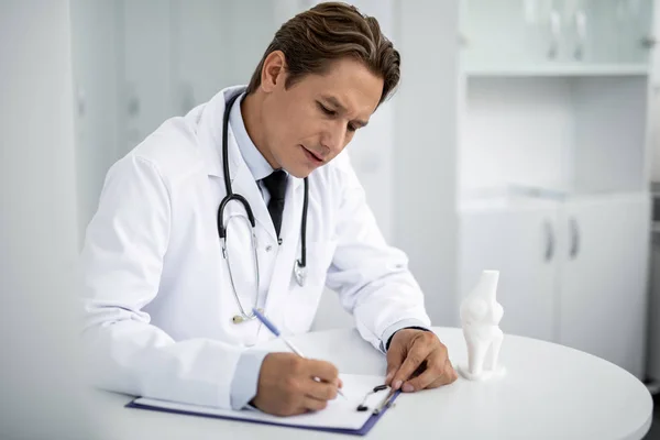 Rauhallinen lääkäri istuu pöydässä ja kirjoittaa reseptejä — kuvapankkivalokuva