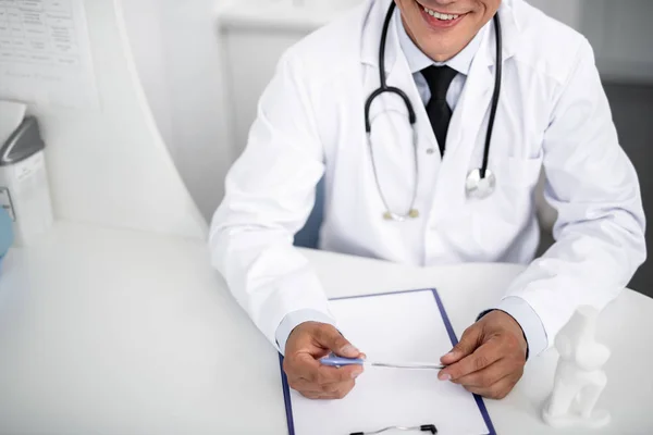 Alegre médico con estetoscopio en el cuello sentado y sonriendo — Foto de Stock