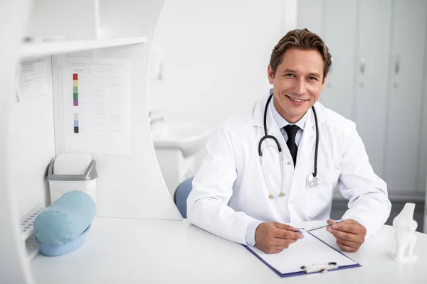 Vyötärö ylös ystävällinen lääkäri hymyilee ollessaan töissä — kuvapankkivalokuva