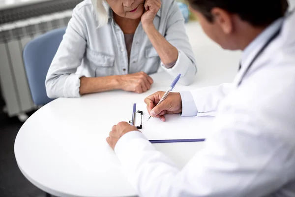 Paciente atento olhando para o médico que escreve a prescrição — Fotografia de Stock