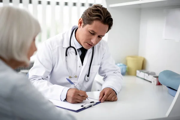 Zorgvuldige beoefenaar notities maken terwijl u luistert naar de patiënt — Stockfoto