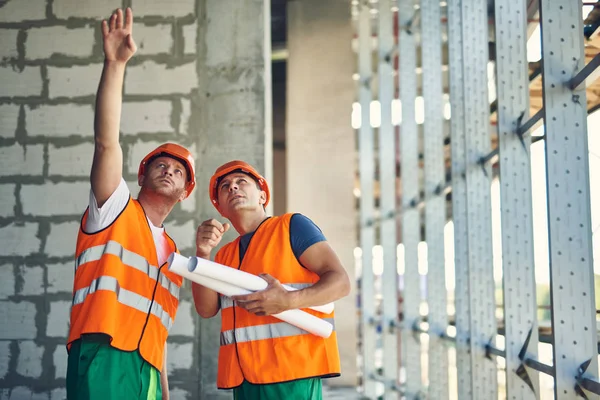 Constructor reflexivo apuntando al techo mientras está de pie con su compañero de trabajo —  Fotos de Stock