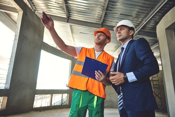 Foreman is showing working construction to his project manager while standing in building