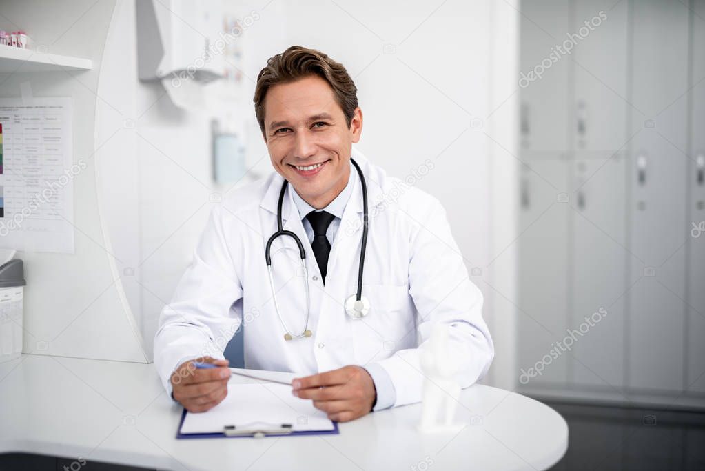 Waist up of happy general practitioner sitting and smiling