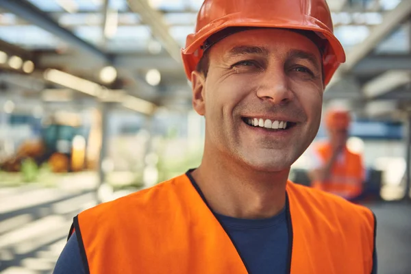 Constructor adulto sonriente se encuentra en el sitio de construcción — Foto de Stock