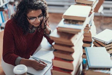 Yığın kitap ile oturan ve yazma neşeli öğrenci