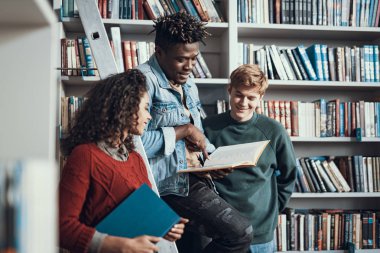 Üç arkadaş kütüphanede okuma sırasında sayfa bakıyor