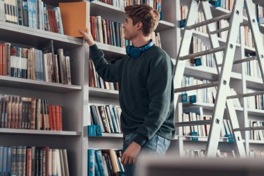 Gülümseyen ve büyük kitap rafa koyarak kendine güvenen öğrenci