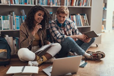 İki genç insanlar kitaplık yanında oturan ve laptop arıyorum