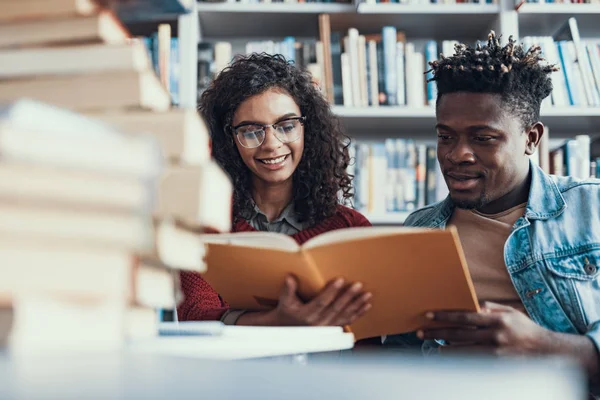 Zwei junge Leute lächeln während sie das Buch lesen — Stockfoto