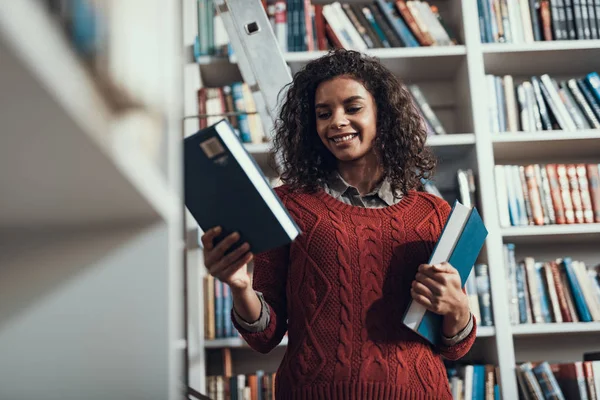 Junge Dame freut sich bei der Buchauswahl in der Bibliothek — Stockfoto