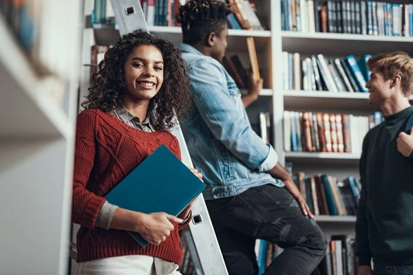 Linda senhora de pé com livro e seus amigos falando no fundo — Fotografia de Stock