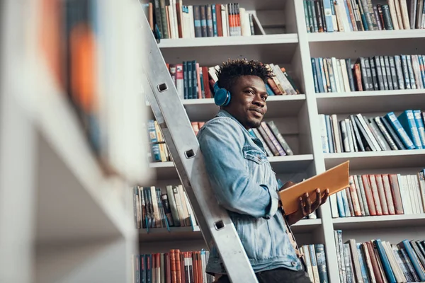 Positiver Schüler, der Musik hört, während er in der Bibliothek ist — Stockfoto