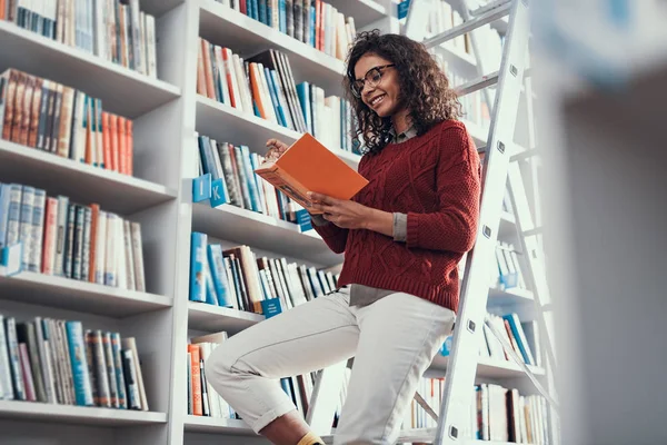 Positiv lächelnde Dame, die auf der Leiter sitzt und liest — Stockfoto