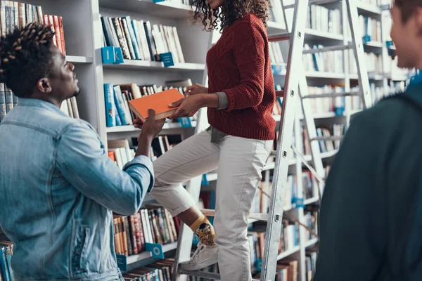 Junge Frau, die auf der Leiter steht und ihrem Freund ein Buch schenkt — Stockfoto