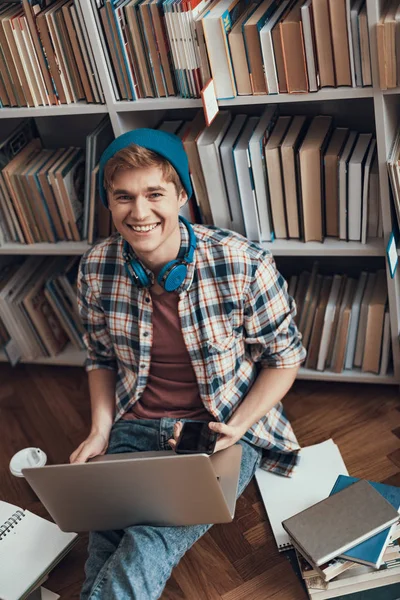 Hüfthöhe eines lächelnden Studenten, der mit seinen Geräten auf dem Boden sitzt — Stockfoto