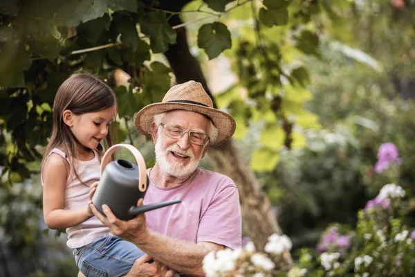 Menina ajudando seu avô regando plantas — Fotografia de Stock
