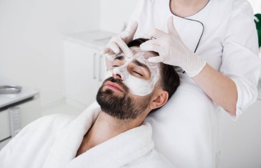 Beyaz kil maskesi adam yüzünde dokunmak dikkatli güzellik uzmanı