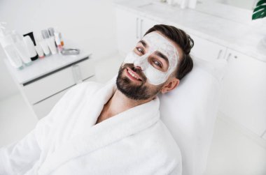 Yararlı beyaz kil maskesi yaparken gülümseyen pozitif adam