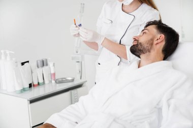 Enjeksiyon ve sakin adam bakarak tutan güzellik uzmanı