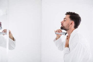 Tek elle boyun ayakta ve tıraş makinesi kullanarak sakin genç adam