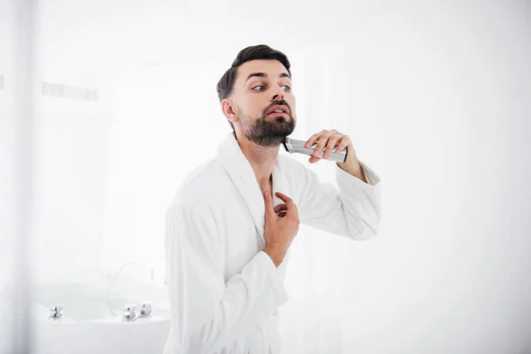 Homem concentrado em roupão de banho raspando cuidadosamente a barba — Fotografia de Stock