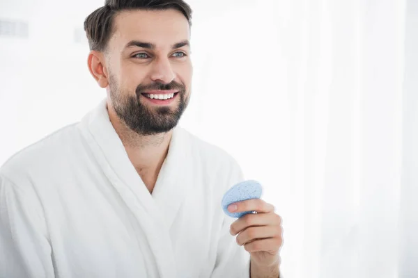 Primer plano de hombre alegre sosteniendo esponja de maquillaje y sonriendo —  Fotos de Stock