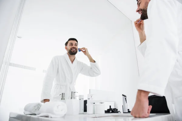 Cintura para cima do homem emocional penteando sua barba e sorrindo — Fotografia de Stock