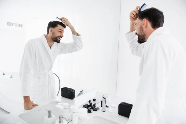 Cintura hacia arriba del hombre emocional peinándose el pelo y sonriendo — Foto de Stock